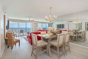 A modern dining area with a glass table, white chairs, and a chandelier. - Hd1605 2 Bedroom Condo by RedAwning (Miramar Beach)