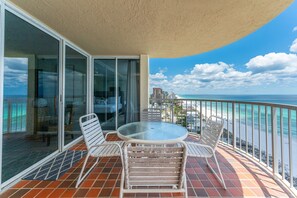 A balcony with a glass door, a round table, and two chairs. - Hd1605 2 Bedroom Condo by RedAwning (Miramar Beach)