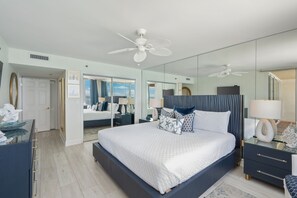 A modern bedroom with a large bed, a ceiling fan, a mirror, and a nightstand. - Hd1605 2 Bedroom Condo by RedAwning (Miramar Beach)