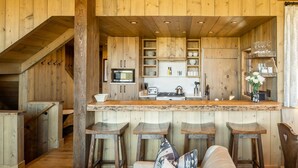 A rustic kitchen with wooden cabinets, a microwave, and a bar area with stools.