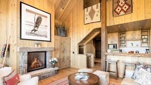 A cozy living room with a fireplace, wooden walls, a dining area, and a kitchen with wooden cabinets.