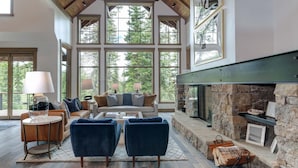 A spacious living room with a stone fireplace, large windows, and a high ceiling.