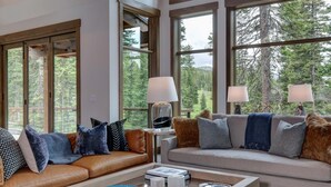 A spacious living room with large windows, leather sofas, and a coffee table.