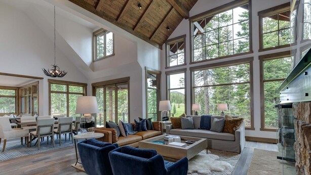 A spacious living room with a high ceiling, large windows, and a fireplace.