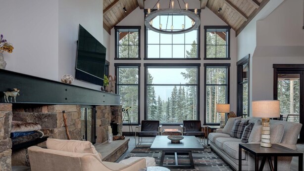 A spacious living room with a stone fireplace, large windows, and a high ceiling. - 6 Jakes Lane 5 Bedroom Home by Moonlight Basin Lodging (Big Sky)