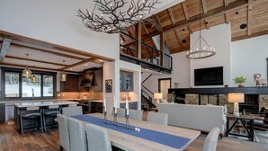 A spacious living area with a high ceiling, a fireplace, and a dining table set for four. - 6 Jakes Lane 5 Bedroom Home by Moonlight Basin Lodging (Big Sky)