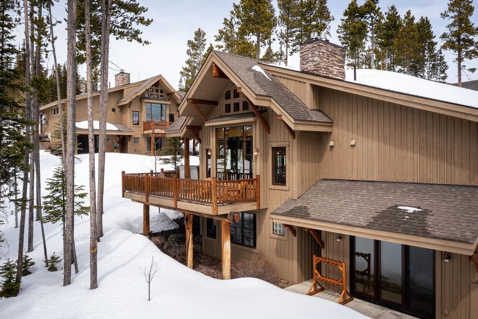 Una cabaña de madera de varios pisos con balcón y ventanas amplias, rodeada de nieve y árboles.