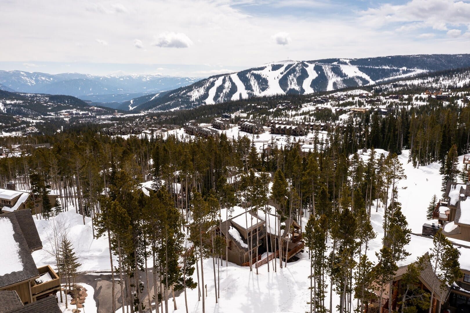 Un paisaje montañoso con terreno cubierto de nieve y un conjunto de cabañas rodeadas de árboles.