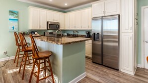 A kitchen with white cabinets, a stainless steel refrigerator, a microwave, and a granite countertop. - Mother Of Pearl - Beach Club #205 4 Bedroom Condo by RedAwning (Dauphin Island)