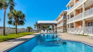 A swimming pool with a covered area, palm trees, and a building with balconies. - Mother Of Pearl - Beach Club #205 4 Bedroom Condo by RedAwning (Dauphin Island)
