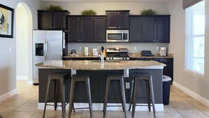 A modern kitchen with dark cabinets, a central island with stools, a refrigerator, microwave, and a coffee maker.