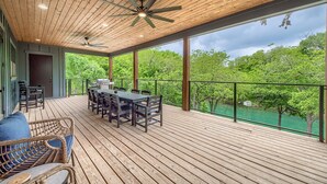 A wooden deck with a table and chairs, a ceiling fan, and a view of trees.
