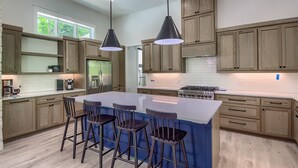 A modern kitchen with wooden cabinets, a large island with bar stools, pendant lighting, and a view of the outdoors.