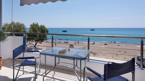 Ein Balkon mit Tisch und Stühlen mit Blick auf einen Strand mit Booten und Menschen.
