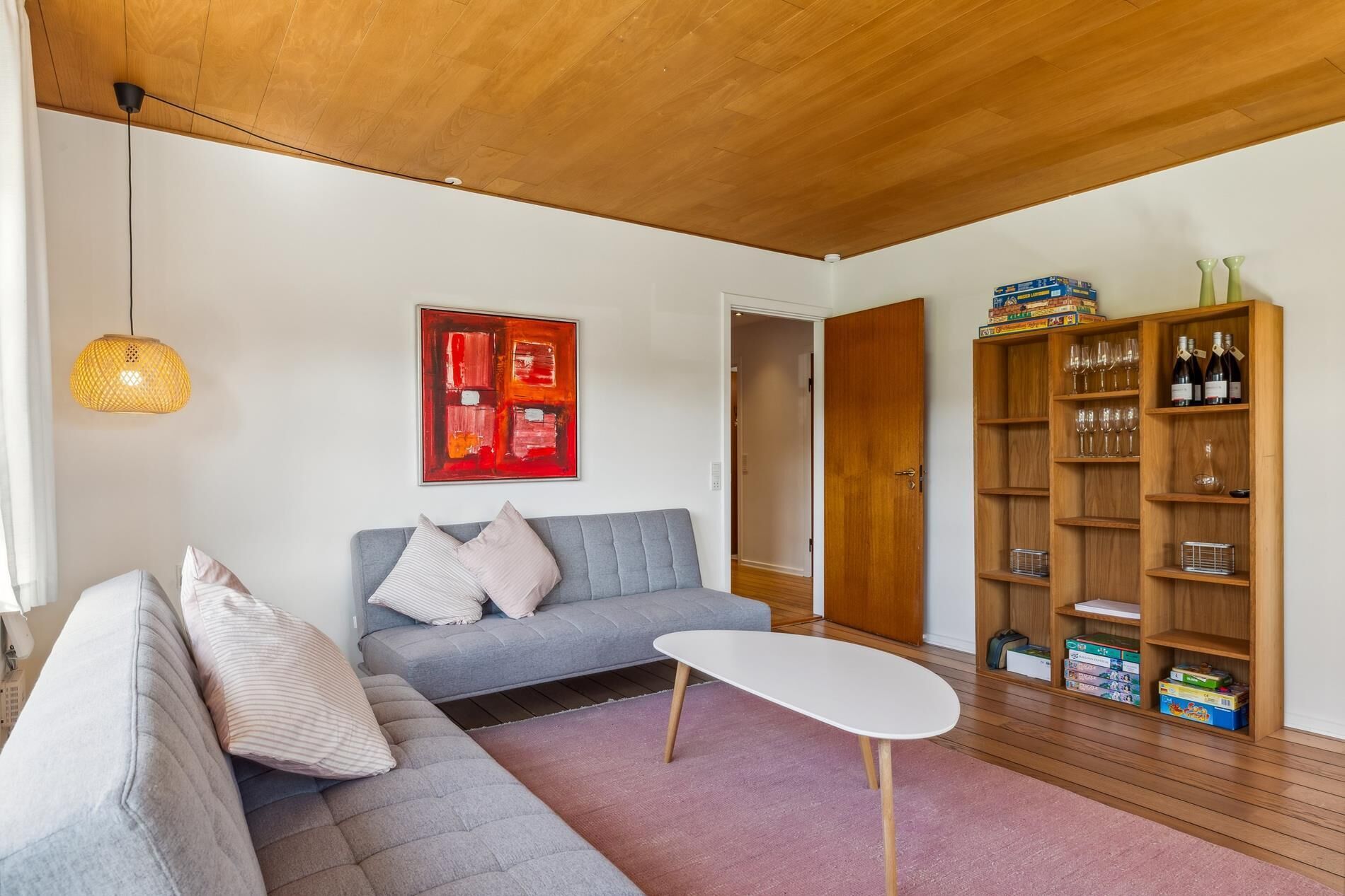 A modern living room with a grey sofa, a white coffee table, and a wooden bookshelf filled with books and wine bottles.