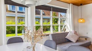 Ein modernes Wohnzimmer mit großem Fenster, einer Couch, einem Esstisch und einer Pendelleuchte.