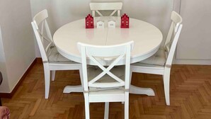 Un coin repas avec une table ronde et quatre chaises blanches, un tapis blanc et quatre tableaux encadrés accrochés au mur.