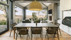 A modern dining area with a large table, wicker chairs, and a hanging light fixture. - Personal Sanctuary, comfort and luxury at every turn (Kiawah Island)