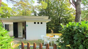 A small, single-story building with a white exterior, a door, and a window. There is a white chair and a table with a vase of flowers outside. - The perfect family retreat-Beahost (Bibione)