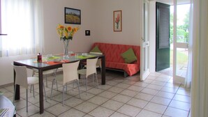 A dining area with a table, chairs, a vase with flowers, a sofa, and a door leading outside. - The perfect family retreat-Beahost (Bibione)