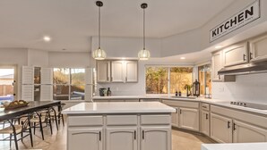 A modern kitchen with white cabinetry, a large island, pendant lighting, and a view of the outdoors. - Heated Saltwater Pool • King Beds • Putting Gr •  Mt Views • Game Rm • Sleeps 11 (Phoenix)