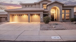 A two-story house with a garage, a driveway, and a well-maintained lawn. - Heated Saltwater Pool • King Beds • Putting Gr •  Mt Views • Game Rm • Sleeps 11 (Phoenix)