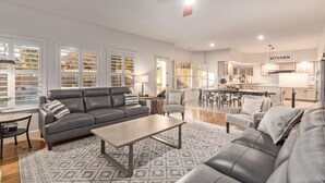 A spacious living room with a grey sofa, a coffee table, and a dining area with a kitchen in the background. - Heated Saltwater Pool • King Beds • Putting Gr •  Mt Views • Game Rm • Sleeps 11 (Phoenix)