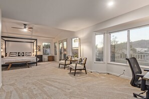 A spacious bedroom with a large bed, a desk, two chairs, and a view of the outside.