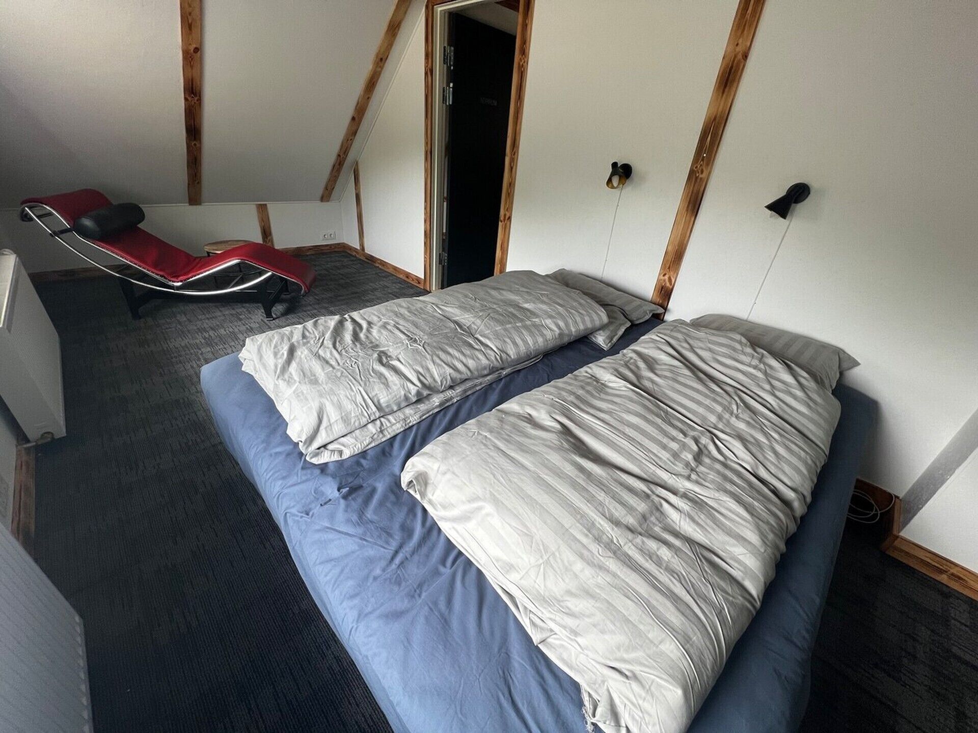 A room with two beds, a red chair, and a wooden ceiling.