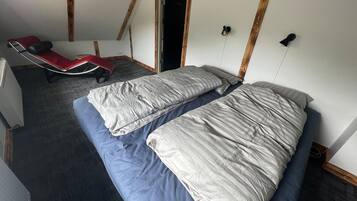 A room with two beds, a red chair, and a wooden ceiling.