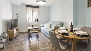 A dining area with a wooden table set for four, a sofa, and a television on a stand. - Sky is blue Granada with private parking included (Granada)