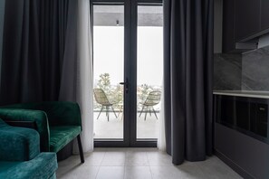 Ein modernes Wohnzimmer mit einem grünen Sofa, einer Schiebetür zu einem Sitzbereich im Freien mit zwei Stühlen und einem Tisch sowie einem eingebauten Kamin.