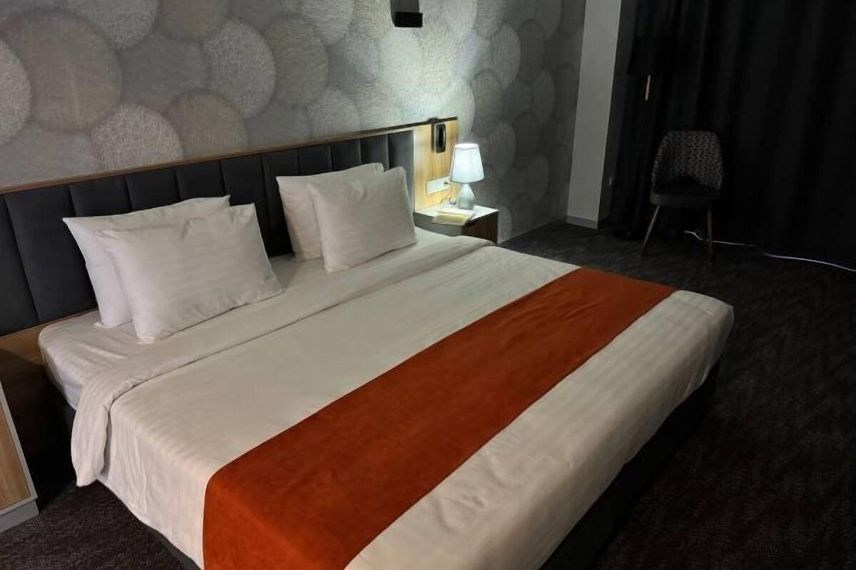 Una habitación de hotel con cama, mesita de noche, lámpara y una silla.