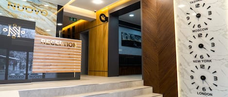 A hotel reception area with a marble wall clock displaying times for Moscow, New York, London, and Tashkent.