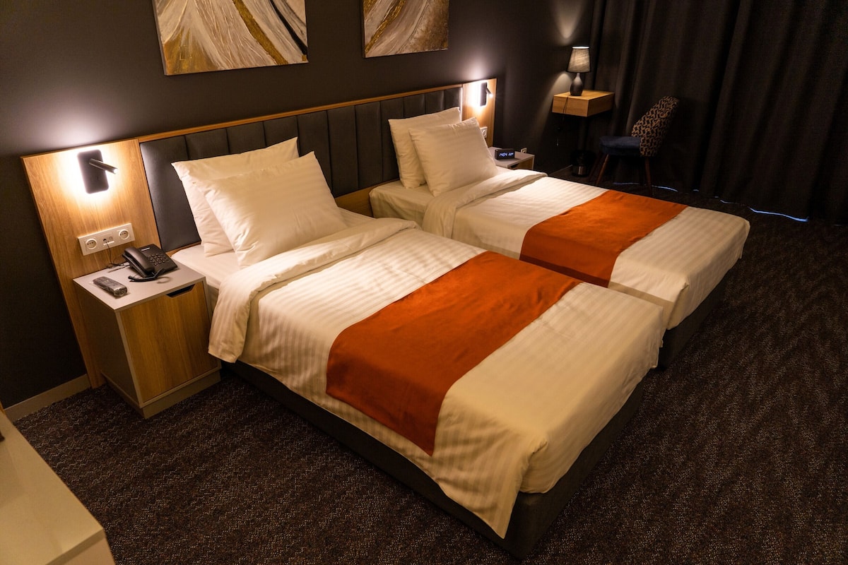 Habitación de hotel con dos camas, una mesita de noche con teléfono, lámpara y una silla.