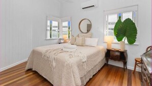 A bedroom with a bed, a round mirror, a potted plant, and a window. - The Grand Queenslander On Turner (Pimlico)