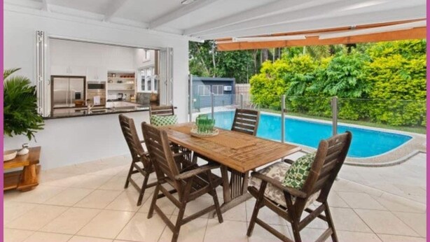 A dining area with a wooden table and chairs, a ceiling fan, and a view of a swimming pool. - The Grand Queenslander On Turner (Pimlico)