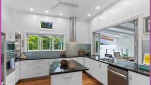 A modern kitchen with white cabinets, a black countertop, and a built-in oven. - The Grand Queenslander On Turner (Pimlico)