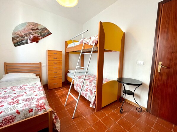 Un dormitorio con una cama individual doble, un aparador, una mesita y un ventilador en la pared.