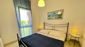 Une chambre à coucher avec un lit, deux tables de chevet avec des lampes, une fenêtre avec des rideaux et un tableau au mur.
