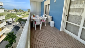 A balcony with a table set for two, a potted plant, and a white air conditioning unit. - Colorful flat by the beach (Porto Santa Margherita)