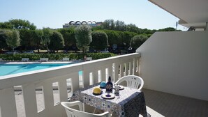 A balcony with a table set for two, overlooking a swimming pool and a building in the background. - Cozy studio with pool (Porto Santa Margherita)