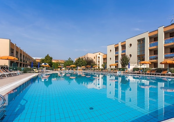 A swimming pool with lounge chairs and umbrellas, surrounded by multi-story buildings with balconies.