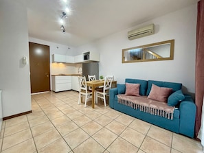 Een gezellig, compacte ruimte met een kitchenette, een eettafel met stoelen, een blauwe bank met plaid en een spiegel aan de muur.