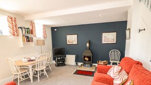 A cozy living room with a fireplace, a dining area with a table and chairs, and a red sofa with patterned cushions. - Well Cottage - 2 bedroom (sleeps 4) (Ashbourne)