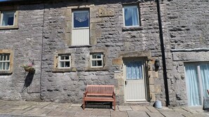 A stone building with multiple windows, a bench in front, and a door with a curtain. - Well Cottage - 2 bedroom (sleeps 4) (Ashbourne)