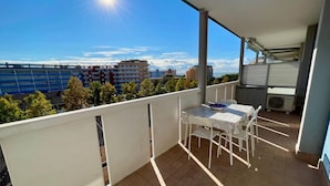 A balcony with a table and chairs, an air conditioning unit, and a view of buildings and trees. - Flat with partial sea view (Porto Santa Margherita)