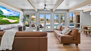 A spacious living room with a large TV, leather sofas, and a view of a pool and outdoor area. - 6BR Luxury Phoenix Home w Pool, Hot Tub, Games (Phoenix)