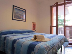 A bedroom with a large bed, a window, and a door leading to a balcony.