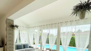 Comedor con mesa de vidrio, sillas blancas y vista a una piscina.